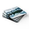 Coaster set with watercolor art print of a mountain, trees and a lake. stacked on a table.