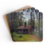 Set of 4 coasters with an image of a log cabin in a forest printed on them. Shown stacked on a table.