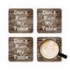 Set of four square coasters with image of wood with water rings on it and text that says 'Don't Ruin My table'. Shown with a mug for scale.
