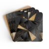 Set of 4 square coasters with a triangle geometric design in black and gold with some gold glitter effect printed on them. Shown stacked on a table.