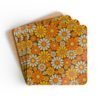 Set of 4 square coasters with 1960's hippie style daisy pattern in orange, yellow, brown and off white colors. Shown stacked on a table.