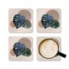Set of four square coasters with a neutral boho design with Monstera leaves. Shown with a mug for scale.