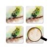 Set of four square coasters with watercolor image of a green and yellow Parakeet printed on each one. They are shown with a mug for scale.