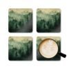 Set of four square coasters with image of misty green and grey forest landscape with layered trees fading into soft mountain fog.